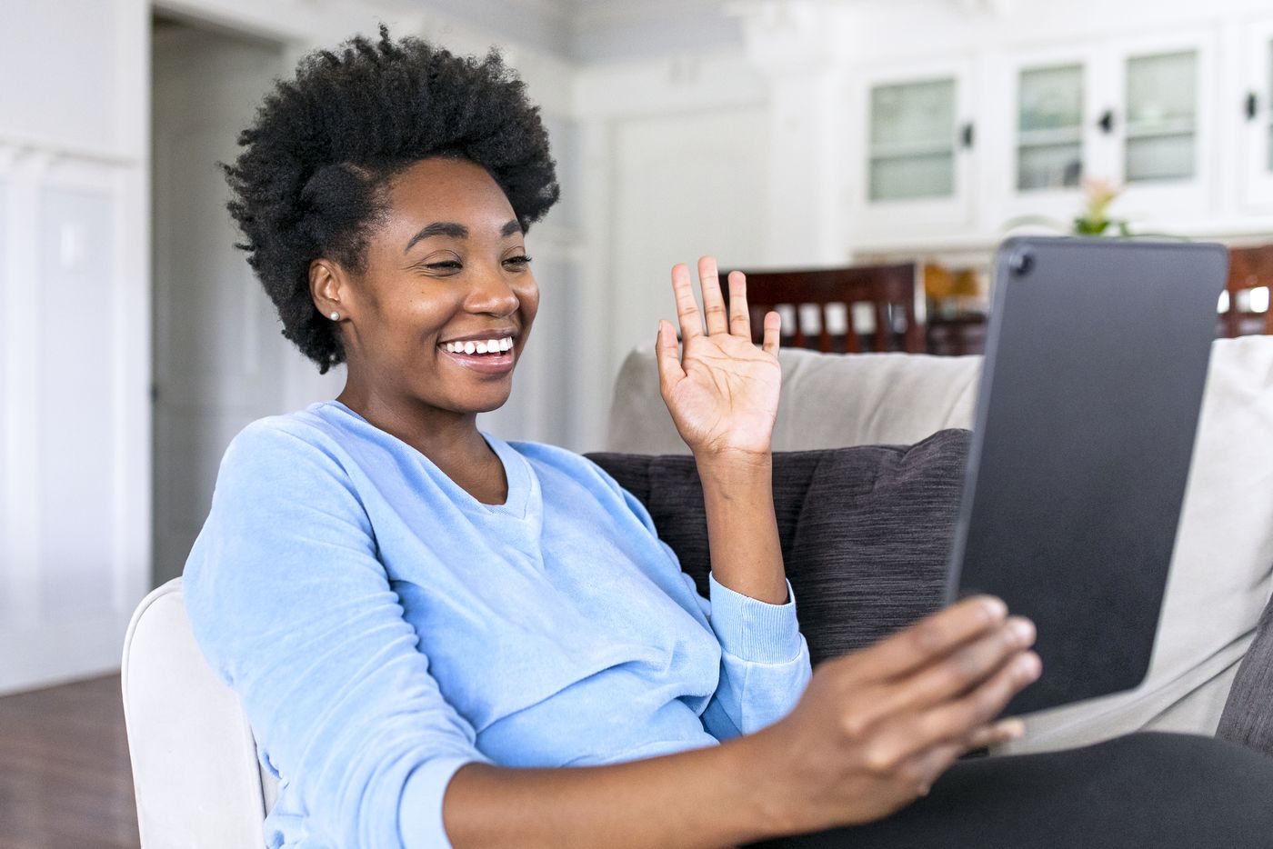 Woman sitting at home on a video call, waving at a tablet screen